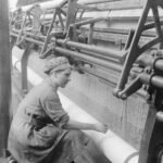 George P. Lewis. El empleo de las mujeres en Gran Bretaña, 1914-1918. Una trabajadora se agacha ante su telar para preparar la urdimbre en una fábrica de encajes de Nottinghamshire. Septiembre de 1918. Dominio público.